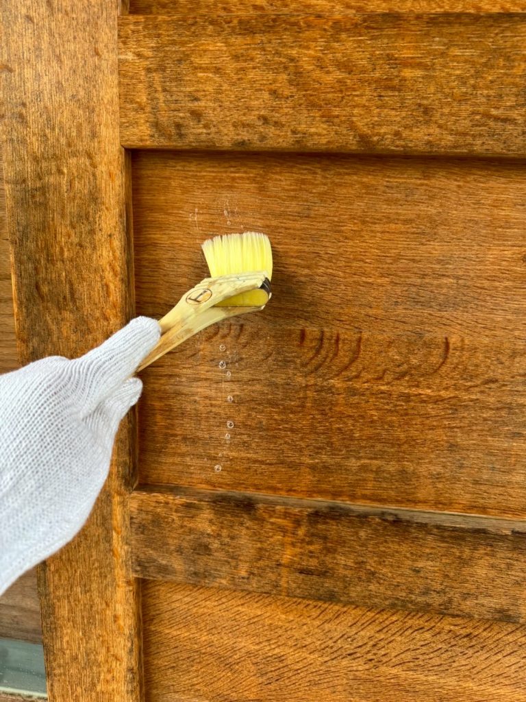 玄関扉に刷毛で洗剤を塗っている